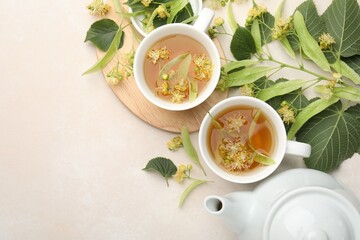 Fresh linden tea in cups, teapot and flowers on white table, flat lay. Space for text