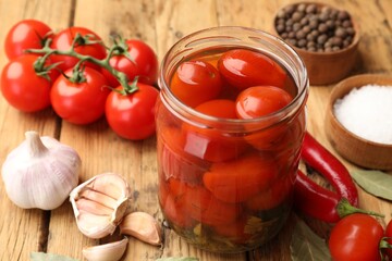 Tasty pickled tomatoes in jar and ingredients on wooden table, closeup