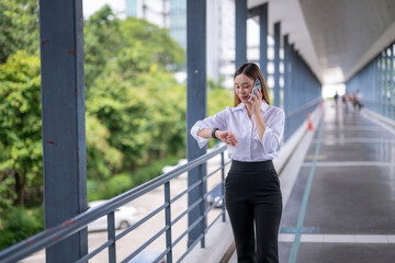 Businesswoman walking and talking on phone while checking time on smartwatch