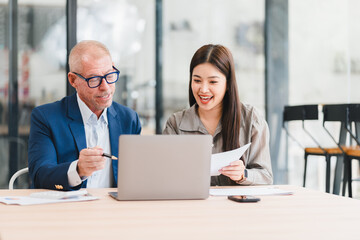 Two business colleagues working together on laptop and documents in modern office, sharing ideas and smiling with positive energy