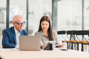 Two businesspeople discussing work with laptop and documents in modern office, showing positive and engaged expressions