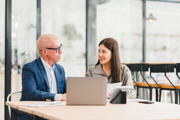 Two businesspeople discussing work with laptop and documents in modern office, showing positive and engaged expressions