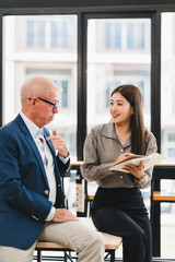 Young woman and senior man having friendly conversation in bright modern office, sharing ideas and notes with smiles, showing positive communication and collaboration