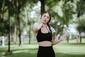Young Asian woman drinking water after exercise, standing outdoors in workout clothes with towel,...