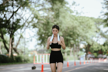 A young woman is jogging outdoors in a park, wearing workout clothes. She is surrounded by nature...