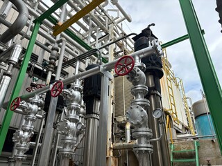 Industrial cooling tower system emitting vapor under blue sky. Heavy-duty piping, valves, and heat exchangers in a manufacturing or refinery plant exterior.