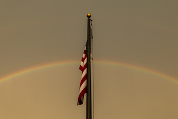 American flag flies proudly with rainbow in background at sunset