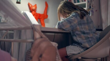 Female kid in casual clothes is sitting at the desk and writing in copybook during doing her homework. Slow motion view of teenage girl studying at home and preparing school task. Education theme - Powered by Adobe