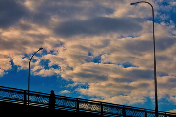 雲の多い空の下の陸橋を渡る女性