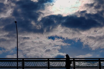 雲の多い空の下の陸橋を渡る女性