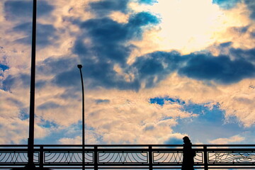 雲の多い空の下の陸橋を渡る女性