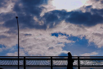 雲の多い空の下の陸橋を渡る女性