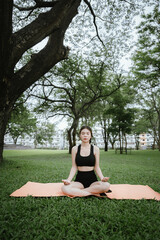 A young Asian woman meditates outdoors for peace, mindfulness, and physical well-being. She feels calm, relaxed, and spiritually connected amidst nature.