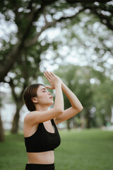 A young woman practices yoga outdoors in a peaceful urban park, promoting wellness, balance, and mindfulness through stretching exercises on a mat surrounded by nature and tranquility.
