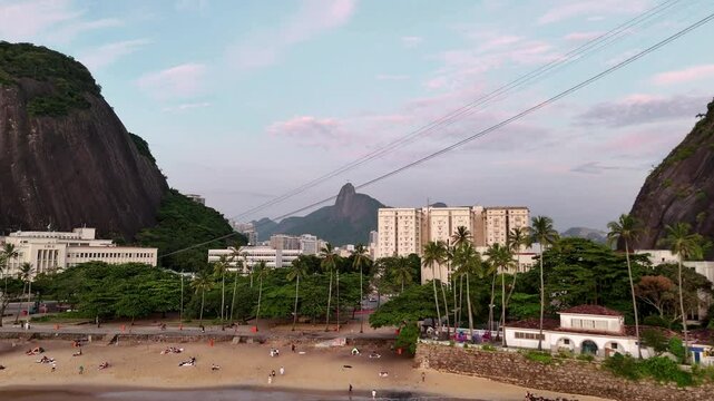 Aerial sunrise view of Praia Vermelha in Rio de Janeiro with tropical palm trees, golden sand, and city skyline beneath soft morning light