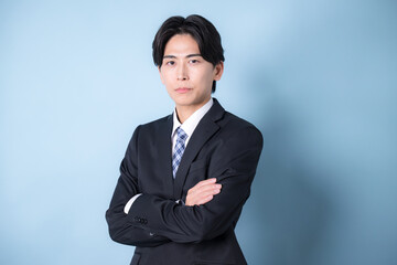カメラ目線でスーツを着たビジネスマンの腕組みの若い男性水色