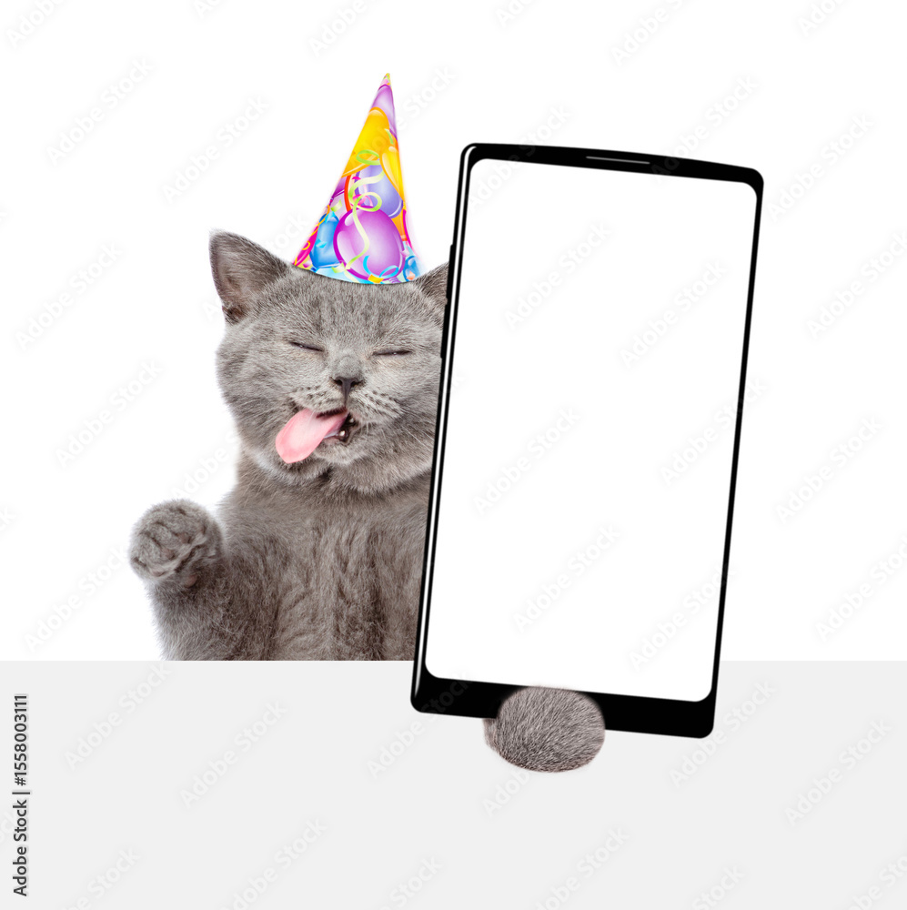 Poster happy licking lips cat wearing party cap shows big smartphone with blank screen above blank white ba