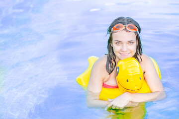 Happy teen girl swimming in the pool with inflatable toy duck . Empty space for text