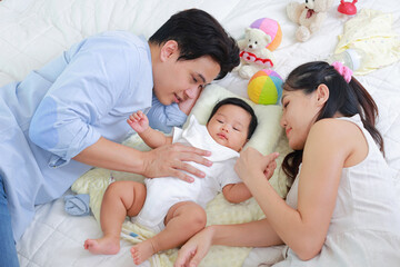 Top view of father and mother hugging their little baby son sleeping on white bed. They are happy. Family concept. Health and life insurance.