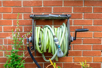garden hose (sun faded green with nozzle) reeled into spool on a red brick wall
