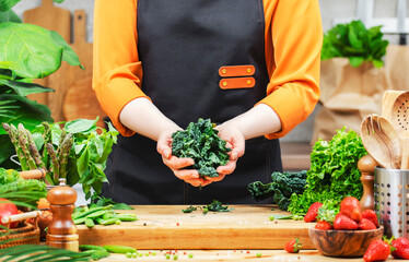 Chef woman holds chopped fresh leafy tuscan kale and vegetables in a sunny kitchen, creating a healthy vegan meal.