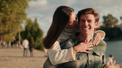 A young couple enjoys a piggyback ride along the Guadalquivir River in Seville, Spain. They laugh and smile, enjoying the beautiful sunset and each other's company. - Powered by Adobe