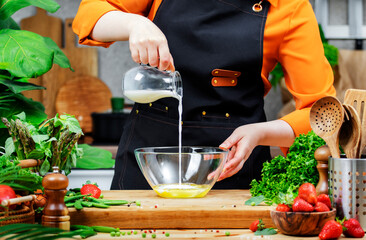 female chef in an orange shirt pours milk into a bowl of fresh ingredients, highlighting her culinary skills and healthy lifestyle.