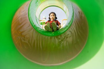 Joyful Child Playing in Colorful Playground Slide Captured from Inside Viewpoint with Bright Green...