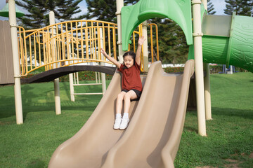 Joyful Child Sliding Down Playground Slide with Excitement in Sunny Outdoor Environment Surrounded...