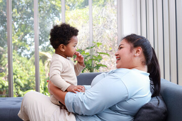 Mother and little son are sitting and relaxing on the sofa at home. They are smiling happily. Family concept. Learning development for 1 year old children.