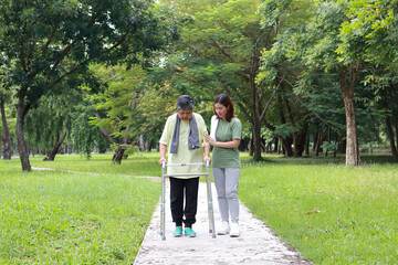 Wide view. Daughter takes care of her elderly mother walking for exercise using a cane to support her while doing physical therapy in an outdoor garden. Health care for the elderly. copy space
