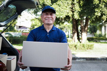 An elderly man in a blue shirt works as a delivery service, holding a box to deliver to a customer at their doorstep. Freight forwarding.