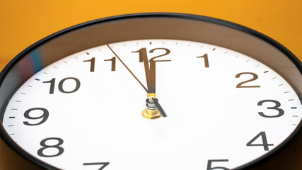 Close-up of a wall clock showing the time exactly at 12 o'clock set against a vibrant orange...