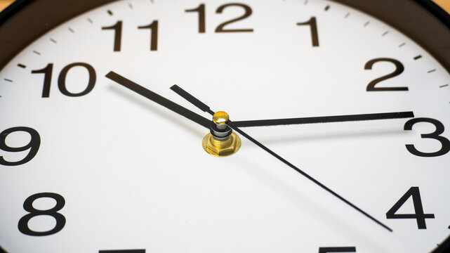 Close-up round wall clock displaying the time 10:14 clean white face with black numerals and hands. - Powered by Adobe