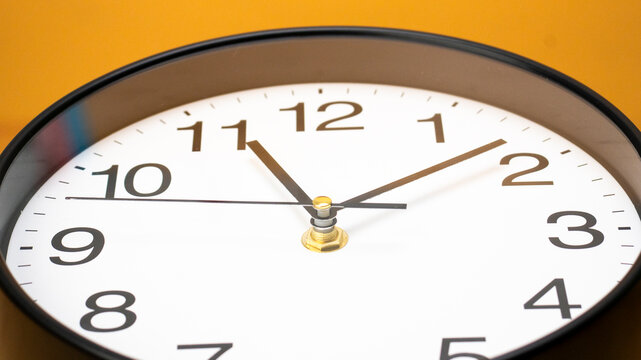 Modern wall clock displaying the time 11:08 clean white face with bold black numerals and hands set against vibrant yellow background.