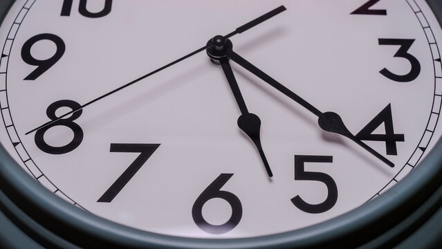 Close-up round wall clock displaying the time 5:22 clean white face with black numerals and hands.