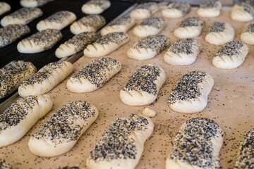 Freshly prepared dough loaves with poppy seeds in a busy bakery plant during morning hours