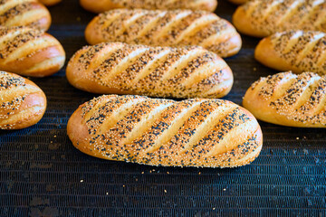Freshly baked bread rolls emerge from the oven in a busy bakery during the morning rush