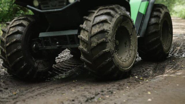 Close-up of powerful wheels of quad bike driving on rural road in mud. Off-road vehicle driving on road washed out by rain.