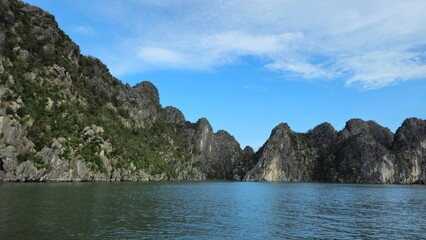Stunning limestone island rising from emerald water in Ha Long Bay, Vietnam, beneath a sky streaked with soft clouds.