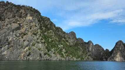 Stunning limestone island rising from emerald water in Ha Long Bay, Vietnam, beneath a sky streaked with soft clouds.