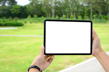 Hands holding digital tablet with blank screen outdoors, ideal for mockup or app promotion in a natural