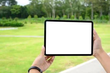 Fotobehang Hands holding digital tablet with blank screen outdoors, ideal for mockup or app promotion in a natural © Prathankarnpap