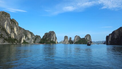 Fototapeta premium A scenic view of calm emerald waters with limestone islets in Ha Long Bay, Vietnam, under a clear blue sky.
