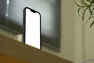 Smartphone with blank white screen standing upright on a wooden surface with soft natural background