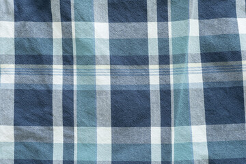 A close-up of a plaid fabric in various shades of blue, teal, and white, creating a classic checkered pattern, showcases the intersecting lines and the texture of