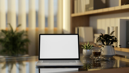 Fototapeta premium Blank screen laptop and coffee cup on glass top wooden table in living room with glass wall's blinds.