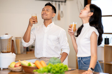 Asian man and woman enjoy drinking a glass of smoothie after making it together at kitchen counter.