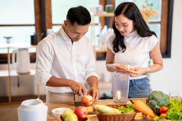 Asian man holding knife woman putting apple cuts in blender making smoothie drink at kitchen counter