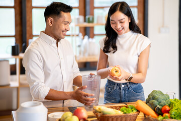 Asian man holding blender jar and woman cutting an apple making smoothie drink at kitchen counter.